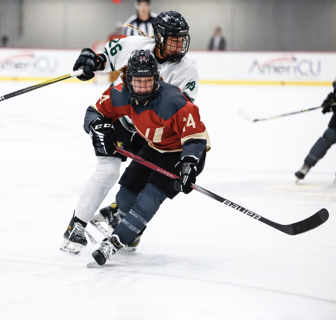 PWHL Montreal player in red and PWHL Boston player in white compete for the puck during a recent preseason matchup.